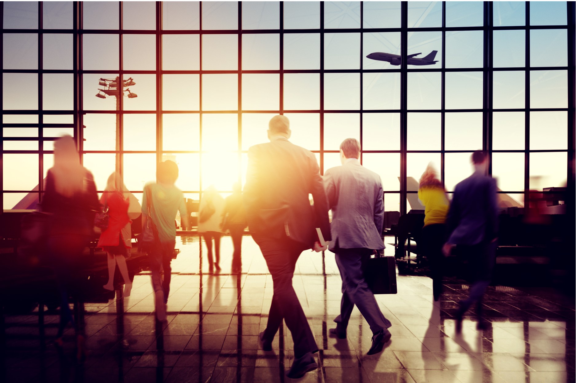 people moving around an airport terminal with a plane in the background