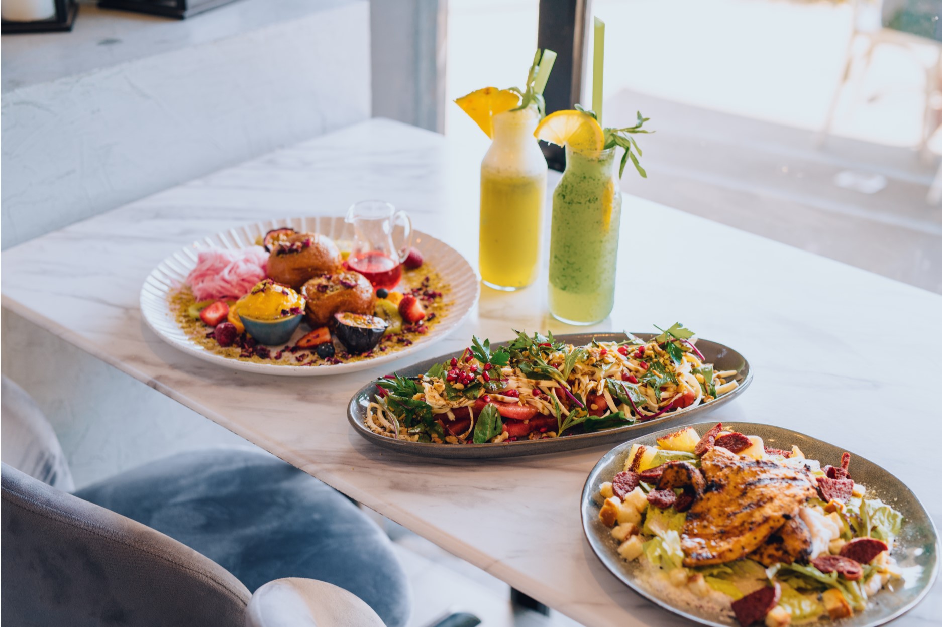 three plates of food and two tropical drinks on a table