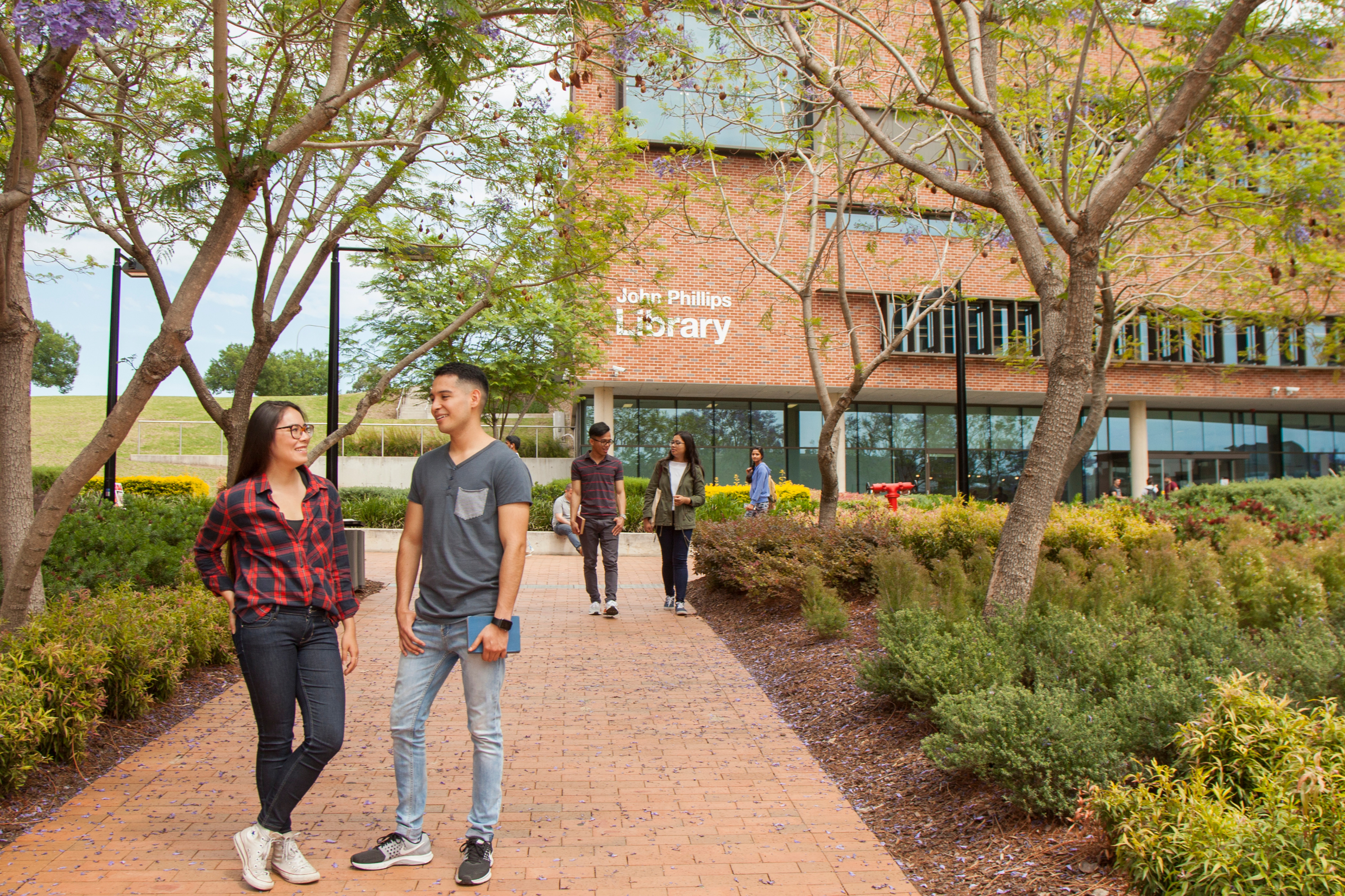 woman and man talking in leafy area outside university building