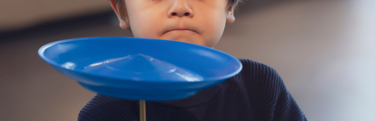 A boy spinning a blue plate on a stick.