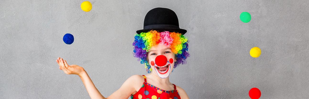 A girl dressed as a clown juggling balls in the air.