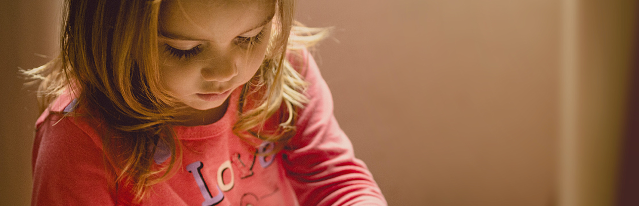 A little girl looking down at a book.