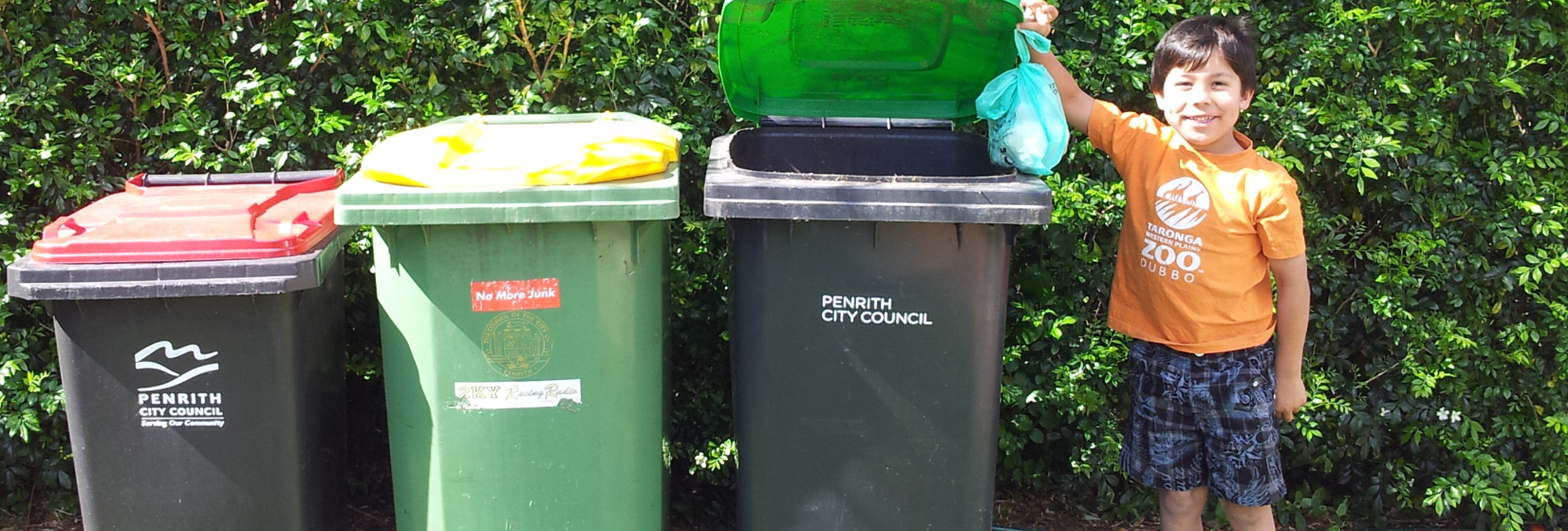 Child holding rubbish bag standing next to three bins